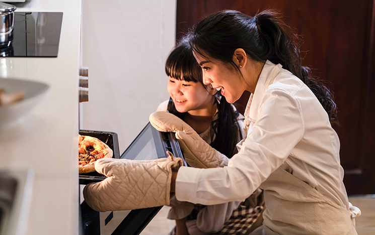 Woman and girl removing food from oven