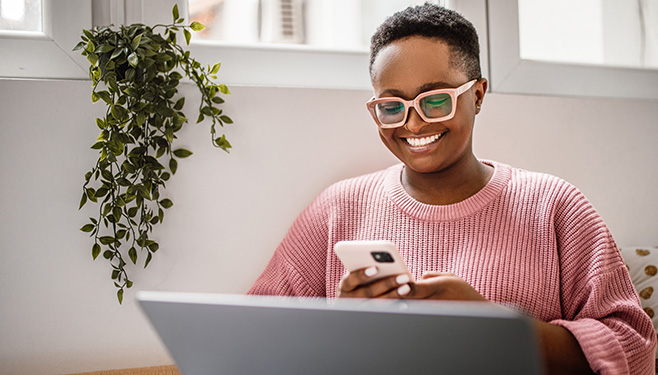 woman sitting in front of laptop looking at phone smiling