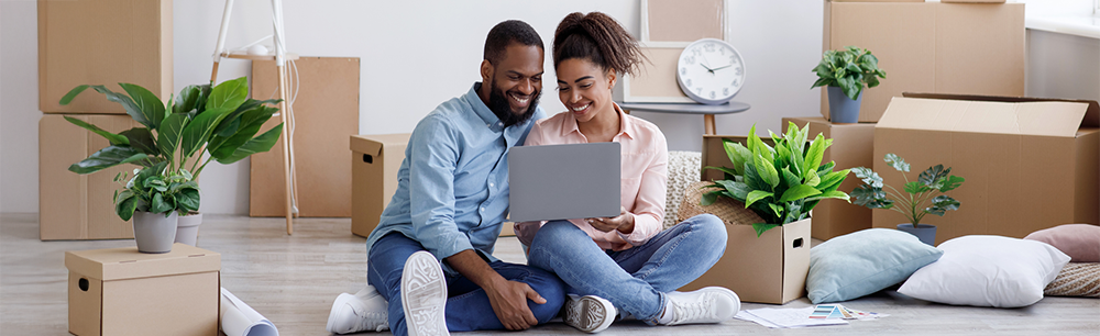 Man and woman looking at laptop sitting on the floor surrounded by boxes