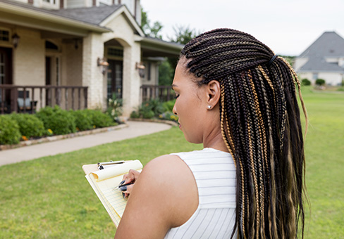 Image of woman writing on clipboard in front of a house